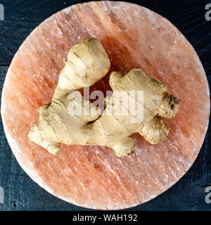 Frischer Ingwer Wurzeln auf persischen rosa Salz board schließen bis auf schwarz Holz- Hintergrund, Asian Food Konzept Stockfoto