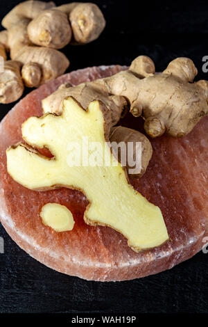 Frischer Ingwer Wurzeln auf persischen rosa Salz board schließen bis auf schwarz Holz- Hintergrund, Asian Food Konzept Stockfoto