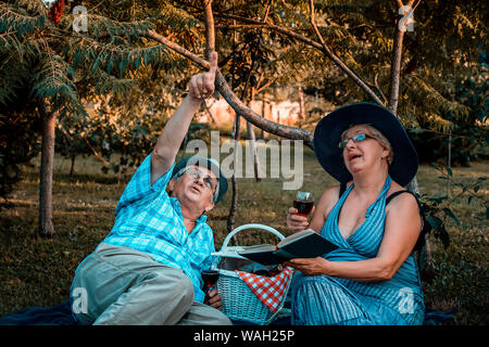 Senior paar Weg, der in die Himmel und Wein trinken und eine tolle Zeit zusammen auf einem Picknick im Park. Stockfoto