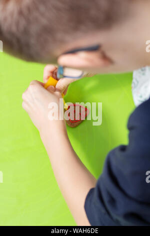 Der junge schmückt ein Zimt Cookie. Er hält eine Tube rot Vereisung in seine Hände und drückt es auf dem Kuchen. Stockfoto