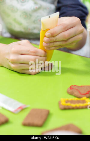 Ein Kind in der Küche. Cookies mit bunter Zuckerglasur verzieren. Die Hände des Kindes drücken Sie die Glasur in Gelb. Stockfoto