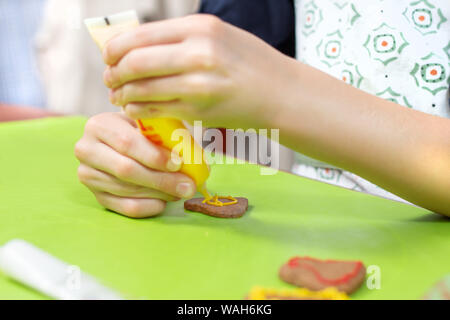 Ein Kind in der Küche. Cookies mit bunter Zuckerglasur verzieren. Die Hände des Kindes drücken Sie die Glasur in Gelb. Stockfoto