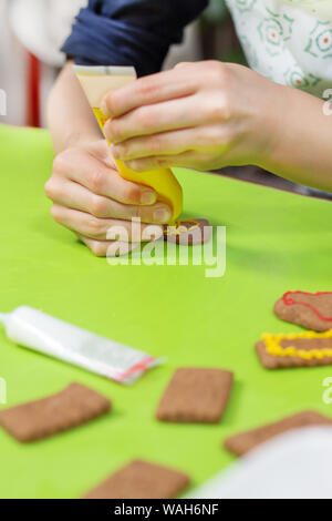 Ein Kind in der Küche. Cookies mit bunter Zuckerglasur verzieren. Die Hände des Kindes drücken Sie die Glasur in Gelb. Stockfoto