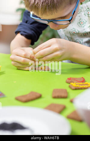 Ein Kind in der Küche. Cookies mit bunter Zuckerglasur verzieren. Die Hände des Kindes drücken Sie die Glasur in Gelb. Stockfoto