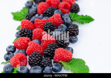 Blaubeeren, Brombeeren, Himbeeren und grüne Blätter auf Weiß isoliert. Stockfoto