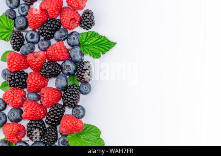 Blaubeeren, Brombeeren, Himbeeren und grüne Blätter isoliert auf Weiss - Flach Foto mit einer Kopie. Stockfoto