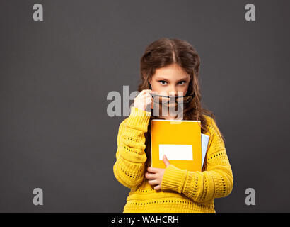 Denken Grimassen ernsthafte Schülerin in Brillen Holding excercise Bücher auf Grau studio Hintergrund. Zurück zu Schule. Der Begriff der Bildung. Schließen Stockfoto