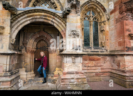 Kaukasische Frau in den 50er steht vor einer gewölbten Holztür in Rosslyn Chapel, Edinburgh, Schottland, Großbritannien, Europa Stockfoto