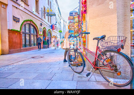 SALZBURG, Österreich - 27. FEBRUAR 2019: Die abgestellten Fahrrad an der Postkarte stand der Souvenirshop in überfüllten Linzergasse, am 27. Februar in Sal Stockfoto