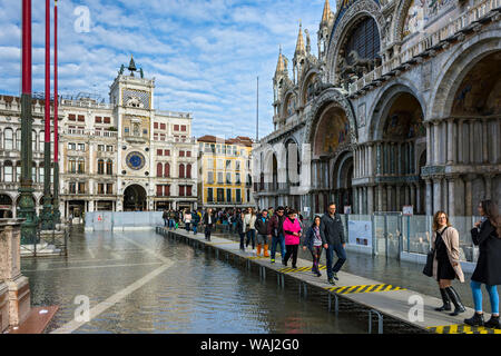 Menschen zu Fuß auf erhöhten Plattformen während der Acqua Alta (hohe Wasser) Fall, vor der Basilika di San Marco, Saint Mark's Square, Venedig, Italien Stockfoto