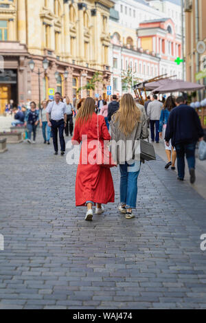 Zwei unkenntlich Mädchen, Freundinnen, die mit dem Rücken zu uns, zu Fuß auf dem Gehweg, das Leben in der Stadt am Nachmittag. Konzept der Jahreszeiten, moderne Stadt, ur Stockfoto