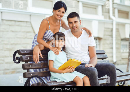 Glücklich lächelnde Familie sitzt auf einer Bank auf der Straße. Stockfoto