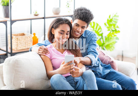 Lächelnd Studenten scrollen Fotos im Smartphone zusammen zu Hause sitzen Stockfoto