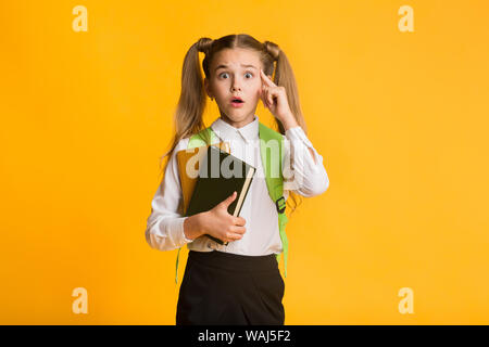 Peinlich Elementary Student auf Kamera Holding Bücher auf gelbem Hintergrund Stockfoto