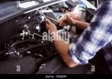 Nahaufnahme von einem Mann Reparieren der kaputten Auto Motor und suchen auch die Ersatzteile auf dem Markt. Stockfoto