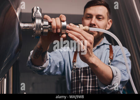 Barkeeper fügt mehr Bier in das Fass mit der Hilfe von Armaturen alle herum, als er einfach neben dem verchromten Barrel steht. Stockfoto