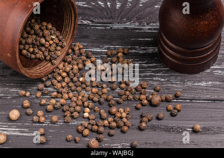 Heap gesamte organische Körner schwarzen Pfeffer auf Holztisch mit Pfeffer Mühle. Stockfoto