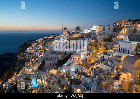 Griechenland, Santorini. Das Dorf Oia in der glühenden - Sonnenuntergang Licht als Lichter der Stadt magic zu dieser kultigen Szene hinzufügen. Stockfoto