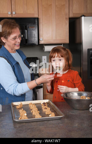Großmutter holding Löffel für 4-jährige Enkelin zu lecken, während Sie Cookies. (MR, PR) Stockfoto