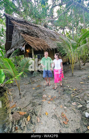 Kosrae, Mikronesien (FSM). Junges Paar Wanderweg von ihren traditionellen Palmen und Bambus thatch Bungalow. Stockfoto