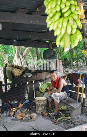 Kosrae, Mikronesien (FSM). Junger Mann kochen Abendessen über eine Kokosnuss Schale Feuer in seiner Küche Hütte. (Redaktionelle nur verwenden) Stockfoto