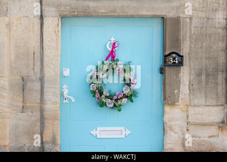 Hellblau Ferienhaus aus Holz Tür mit einem silk Blumen Kranz und Pink Ribbon. Winchcombe, Cotswolds, Gloucestershire, England Stockfoto