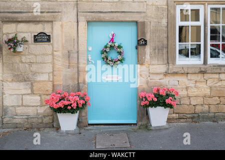 Hellblau Ferienhaus aus Holz Tür mit einem silk Blumen Kranz und Pink Ribbon. Winchcombe, Cotswolds, Gloucestershire, England Stockfoto