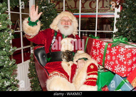 Santa Claus in seinem Schlitten durch eingepackte Geschenke umgeben und winkend. (MR) Stockfoto