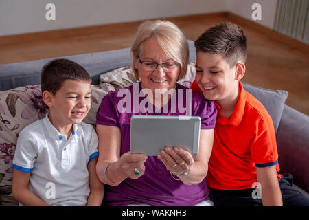 Großmutter mit ihren Enkel auf dem Sofa zu Hause. Oma und Kinder nehmen selfie. Großmutter mit Kindern über elektronische Register Stockfoto