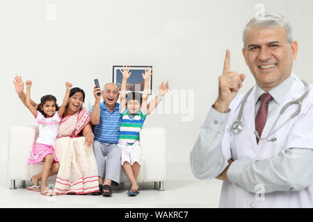 Der Arzt zeigt nach oben, während die Familie im Hintergrund Fernsehen sieht Stockfoto