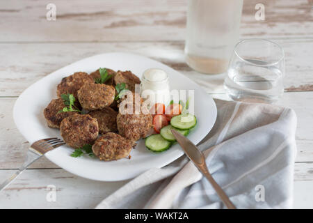 Saftige köstliche Fleisch Schnitzel in eine weiße Platte auf hellem Holztisch. Metballs gebraten serviert mit Tomaten und Gurken und Sauerrahm. Stockfoto
