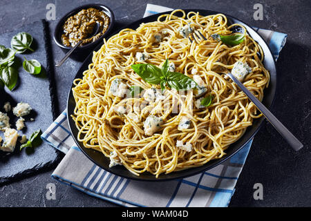 Close-up von leckeren Spaghetti mit Basilikum Pesto und Blauschimmelkäse auf eine schwarze Platte auf einer konkreten Tabelle mit Pesto in einem schwarzen Schüssel, italienische Küche, hor Stockfoto