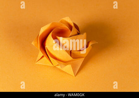 Orange origami Rose auf orangem Hintergrund. Japanische Kunst des Papierfaltens. Flache quadratische Blatt Papier in eine fertige Skulptur übertragen. Stockfoto