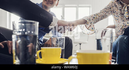 Drei Geschäftsleute bumping Fäuste im Einvernehmen und Zusammenarbeit, wie sie an einem Tisch in einem hellen Büro sitzen. Stockfoto