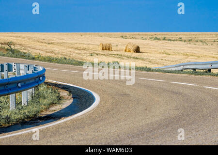 Runde briketts mit Stroh nach der Ernte von Weizen auf einem Feld in der Nähe von eine asphaltierte Straße Stockfoto