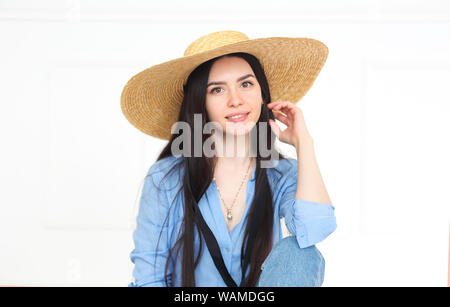 Schöne lächelnde Frau mit Strohhut und blaues T-Shirt mit Kamera und auf hellen Hintergrund posiert Stockfoto