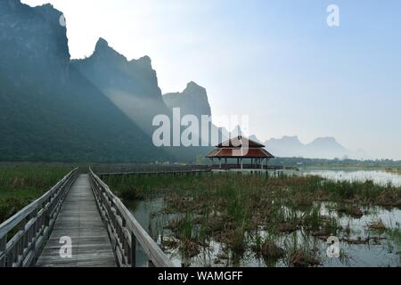 Khao Sam Roi Yot, Holzbrücke und Pavillon, Sun Beam heraus schießen aus hinter Kalkstein Berg Reflexionen auf See, Thailand Stockfoto