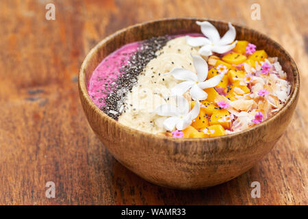 Tropisches Frühstück Fruit Smoothie Schüssel. Gesunde Mango und Banane essen in hölzerne Schüssel auf dem Tisch. Exotische Vegane frische Getränk mit Blumendekoration. Mornin Stockfoto