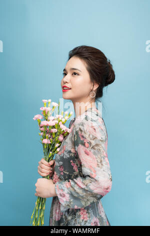 Attraktive Asien Frau in romantisches Kleid mit Blumenstrauß über blauer Hintergrund Stockfoto
