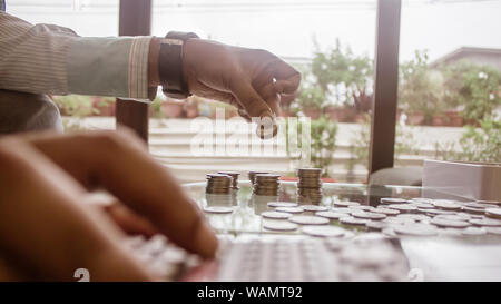 Bild des Geschäftsmannes Zählen von Münzen mit Rechner am Schreibtisch im Büro. Unternehmer Hand Münzen am Stack. Wirtschaft Finanzen Einsparungen und Investoren Stockfoto