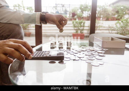 Bild des Geschäftsmannes Zählen von Münzen mit Rechner am Schreibtisch im Büro. Unternehmer Hand Münzen am Stack. Wirtschaft Finanzen Einsparungen und Investoren Stockfoto