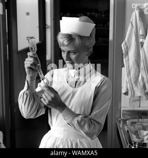 Krankenschwester in den 1960er Jahren. Eine Frau in einer Krankenschwester uniform ist die Vorbereitung einer Injektion und saugt die Flüssigkeit aus einer Flasche Medizin in einer Spritze aufgezogen. september 1963. Stockfoto