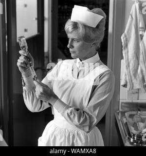 Krankenschwester in den 1960er Jahren. Eine Frau in einer Krankenschwester uniform ist die Vorbereitung einer Injektion und saugt die Flüssigkeit aus einer Flasche Medizin in einer Spritze aufgezogen. september 1963. Stockfoto