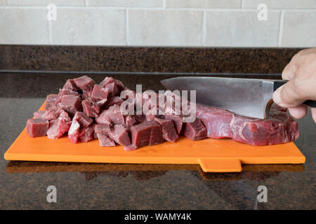 Mann mit nife Schneiden ein mageres Stück Fleisch in Stücke schneiden in der Küche ein Fleischgericht vorzubereiten Stockfoto