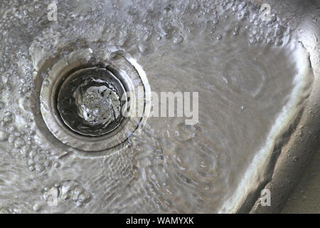 Das Wasser im Waschbecken fließt in den Abfluss. Edelstahl Wasser mit Wasser. Stockfoto