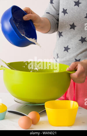 Frau, die Teig für Muffins. Das Mischen von Mehl, Zucker, Eier und andere Zutaten aus bunten Schüsseln. Hausgemachte Speisen, Backen zu Hause. Stockfoto