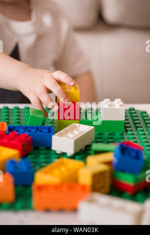 In der Nähe der Hände Kind spielen mit bunten Kunststoff Ziegel am Tisch. Kleinkind, das Spaß und Gebäude aus hellen Konstruktor Steine. Anfang l Stockfoto