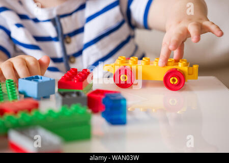 In der Nähe der Hände Kind spielen mit bunten Kunststoff Ziegel am Tisch. Kleinkind, das Spaß und Gebäude aus hellen Konstruktor Steine. Anfang l Stockfoto