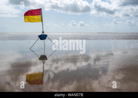 Eine rote und gelbe lebensrettende Flagge gegen einen bewölkten Himmel Setup von Rettungsschwimmern in Pendine, Wales Stockfoto