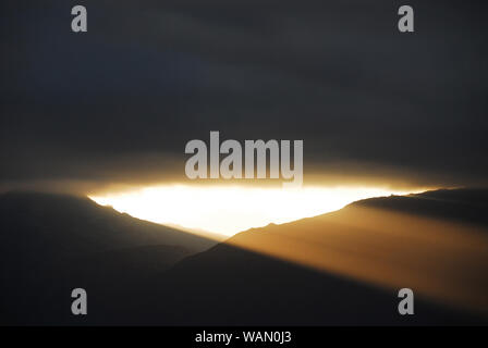 Eine erstaunliche Himmel. Schwarze Gewitterwolken über die Hügel lange genug parted ein Strom des lebendigen, goldenes Sonnenlicht durch in einem großen Kontrast Strahl zu ermöglichen. Stockfoto